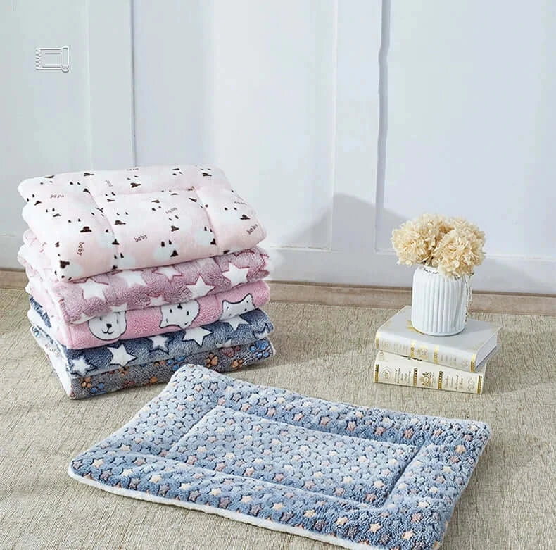 Stack of cozy flannel pet sleeping mats in various colors and designs, featuring a soft, warm surface for pets.