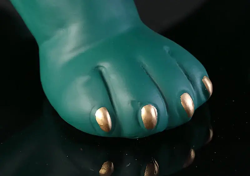 Close-up of the textured green paw of a bulldog resin statue with shiny gold claws, showing intricate details.