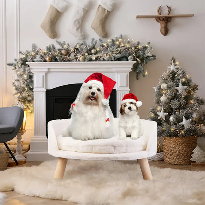 Two dogs wearing Santa hats sitting on a luxury plush cat bed by a cozy fireplace and decorated Christmas tree.